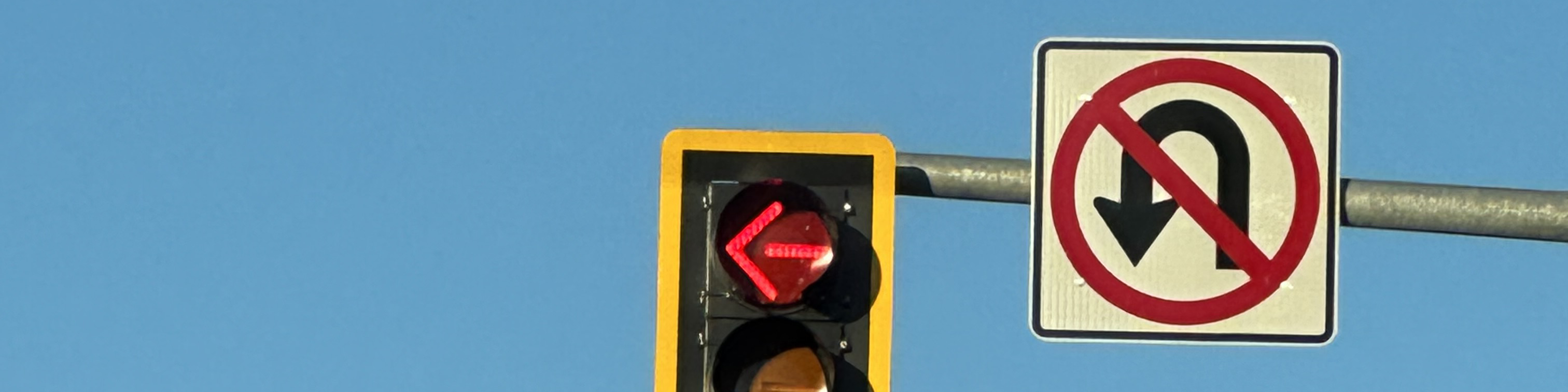 The top-half of a traffic light, bordered in yellow, and a U-turn sign, contrasted against a light blue sky